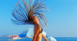 Österreicher buchen wieder mehr Reisen! Reisen: Frau am Strand, wirft Kopf mit Boxbraids zurück