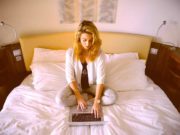 Eine gute Hotelnacht an 365 Tagen im Jahr Ruhige Hotelnacht stärkt Körper, Gest und Seele: Ein junge Frau sitzt auf dem Hotelbett mit ihrem Laptop
