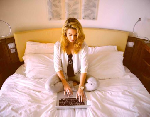 Eine gute Hotelnacht an 365 Tagen im Jahr Ruhige Hotelnacht stärkt Körper, Gest und Seele: Ein junge Frau sitzt auf dem Hotelbett mit ihrem Laptop