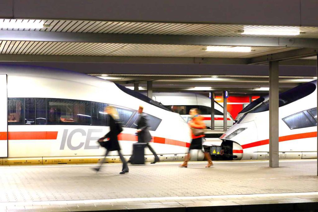 Mit dem Zug statt mit dem Flugzeuge: Reisende gehen am Bahnsteig vorbei an zwei geparkten ICE-Zügen
