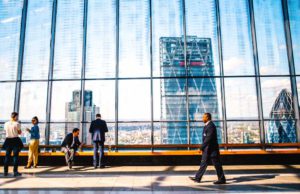 Effiziente Dienstreisen, reduzierte Ausgaben Effiziente Dienstreisen: Bahnhofshalle mit großer Glasfront. Davor stehen Personen und ein Mann schreitet nach links. Im Hintergrund ist ein Hochhaus zu sehen