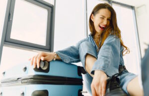 So steht es um die Reisefreiheit in Österreich Das Fluggepäck richtig packen: Lachende Frau sitzt neben ihrem gepackt blauen Koffer