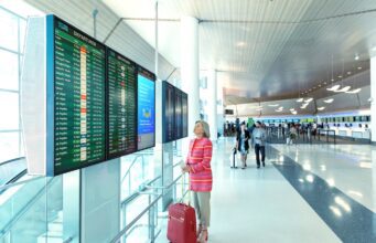 Frauen auf Alleinreisen: Wie fühlen sie sich? Frauen auf Alleinreisen: Eine Frau am Flughafen vor einer Anzeigetafel mit Handgepäck