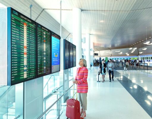 Frauen auf Alleinreisen: Wie fühlen sie sich? Frauen auf Alleinreisen: Eine Frau am Flughafen vor einer Anzeigetafel mit Handgepäck