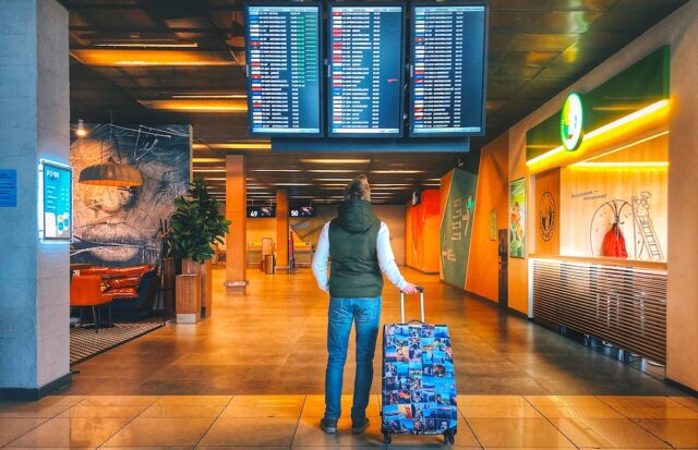 Snus im Handgepäck? Mann mit Koffer am Flughafen, blickt auf Anzeigetafel