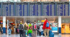Flughafen München startet in den Sommer Evaneos beendet Angebot mit Kurzreisen: Bild zeigt Reisende mit Gepäck vor der Abflugtafel auf dem Flughafen München beim Einchecken