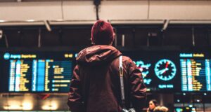 Travellyze-Studie: Reisebranche im Aufwind Travellyze-Studie: Reisebranche im Aufwind: Bild zeigt Mann am Flughafen mit Kamera vor Abfluganzeige