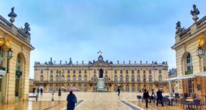 Nancy: Schatzkiste im Herzen Lothringens Bild zeigt die Herzogstadt bei Regen. Ein Mann geht auf ein riesiges Schloss zu