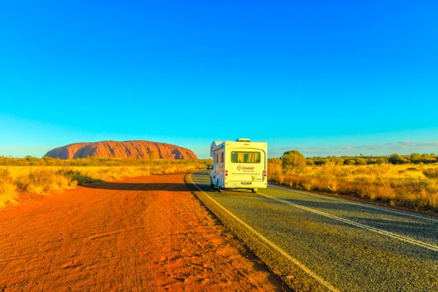 Bis zeigt ein Wohnmobil auf einer Straße zum roten Uluru Ayers Rock im rotem Outbakc von Australien