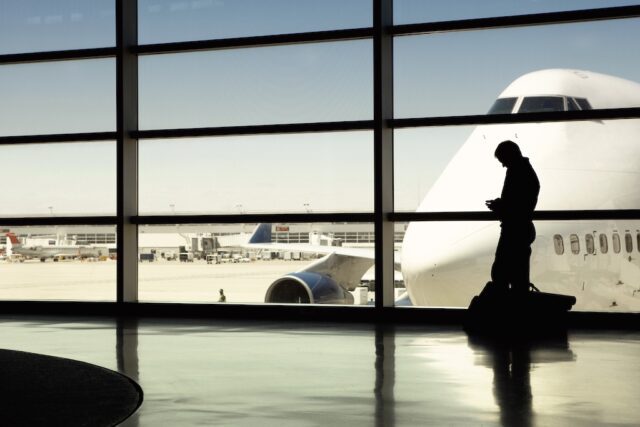 Wartezeiten clever überbrücken: Bildzeigt einen Geschäftsreisenden am Flughafen mit Blick auf ein großes Flugzeug auf dem Flugfeld
