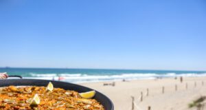 Paella-Köche für Weltmeisterschaft gesucht Paella-Köche für die Paella-WM gesucht: Bild zeigt links eine Paella und im Hintergrund Strand und Meer in Spanien