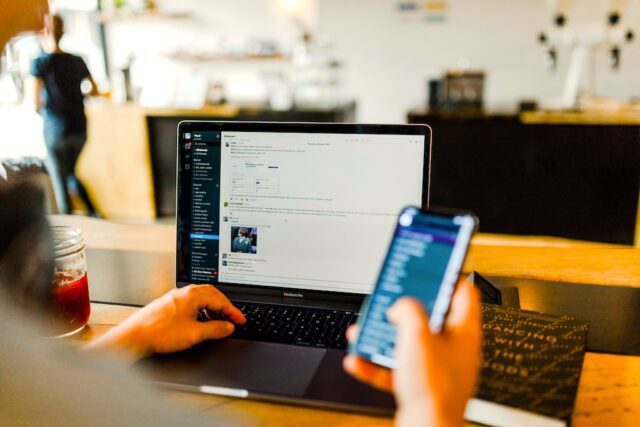 Mitarbeiter-App soll bei Personalmangel helfen: Bild zeigt eine Person vor einem Laptop und mit einem Handy in der Hand