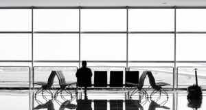 DIN ISO 31030: Wozu brauche ich denn das? DIN ISO 31030 ist vielen Geschäftsreisenden unbekannt. Bild zeigt einen Business Traveler, der allein auf einer Bank im Flughafen sitzt und auf das Vorfeld blickt