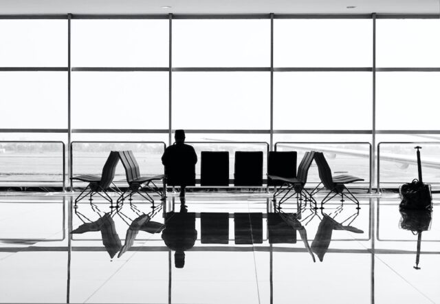 DIN ISO 31030 ist vielen Geschäftsreisenden unbekannt. Bild zeigt einen Business Traveler, der allein auf einer Bank im Flughafen sitzt und auf das Vorfeld blickt