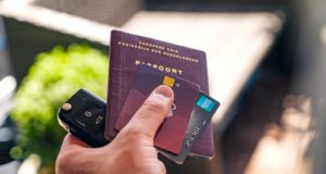Sind Kreditkarten-Reiseversicherungen gut? Bleisure Travel wird zum Hit. Bild zeigt eine Hand, die einen Reisepass, Kreditkarten und einen Autoschlüssel hält