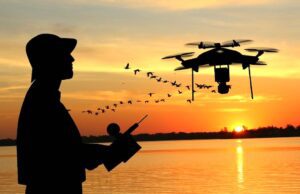 Wenn Drohnen im Urlaub in die Luft gehen Mit einer Drohne im Ausland fotografieren: Bild zeigt einen Mann mit Hut bei Sonnenuntergang, der mit einer Drohne Luftaufnahmen an einem Strand macht