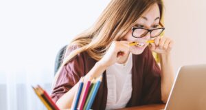 Reiseabrechnungen sind ein „Pain Point“ lReiseabrechnungen sind ein Pain Point: Bild zeigt eine Frau vorm Laptop mit einem Bleistift zwischen den Zähnen bei der Abrechnung ihrer Spesen