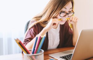 Reiseabrechnungen sind ein „Pain Point“ lReiseabrechnungen sind ein Pain Point: Bild zeigt eine Frau vorm Laptop mit einem Bleistift zwischen den Zähnen bei der Abrechnung ihrer Spesen