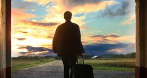 Welche Reiseversicherung ist zu empfehlen? Welche Reiseversicherung? Bild zeigt einen Mann mit Koffer im Gegenlicht. Er geht durch ein Tor