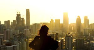 Business of Travel: Vision für Geschäftsreisen Business of Travel und die neue Vision für Geschäftsreisen: Bild zeigt eine Frau im Gegenlicht der untergehenden Sonne, die auf mehrere Wolkenkratzer in einer Stadt blickt