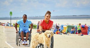 Barrierefrei in Deutschland auf Reisen gehen Barrierefrei reisen: Bild zeigt einen Mann und eine Frau im Rollstuhl mit einem Hund am Strand von Langeoog