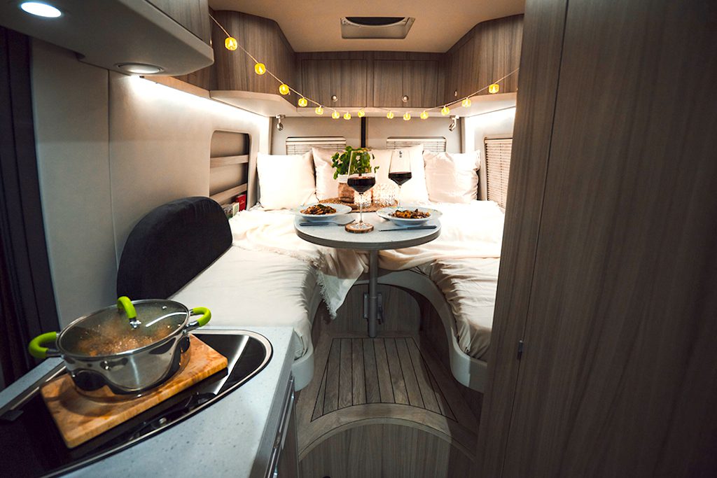 Reisemobile der neuen Art: Bild zeigt das Innere eines Wohnmobils mit Küche, Bett und Tisch