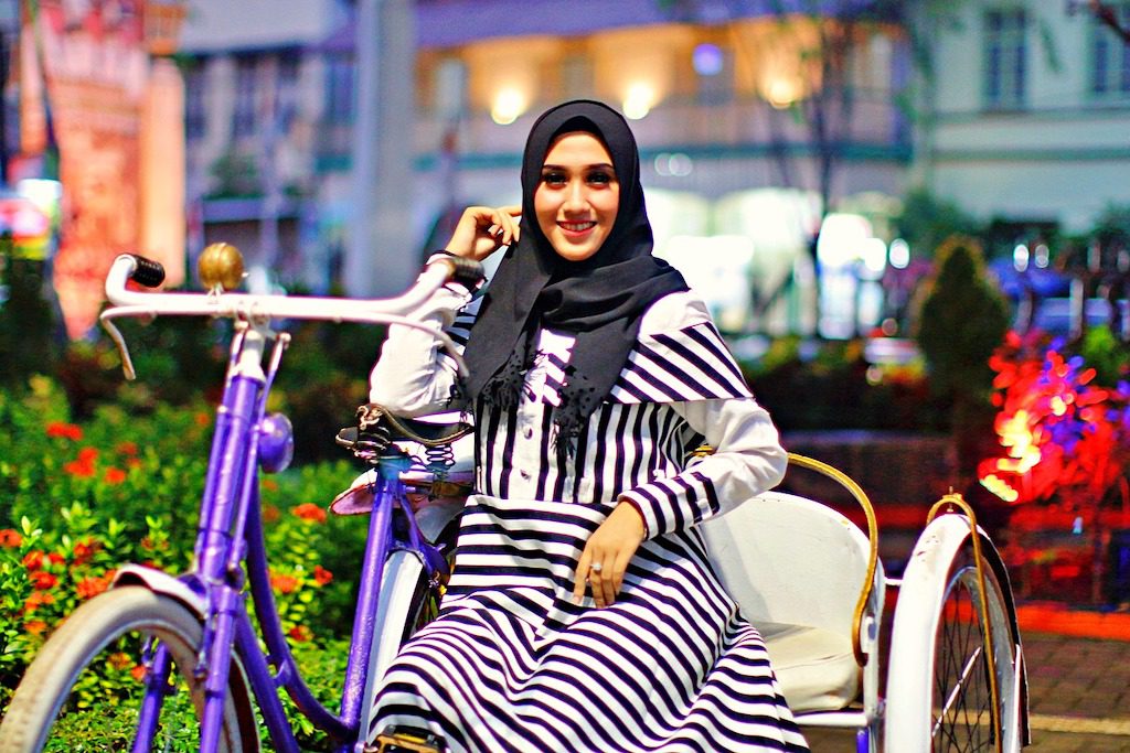 Mode für Muslimas: Bild zeiht eine junge Frau mit schwarzem Kopftuch in einer Rikscha