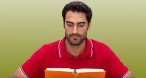 Sprachbarrieren im Tourismus überwinden Sprachbarrieren im Tourismus überwinden: Ein bärtiger Mann mit rotem T-Shirt sitzt mit aufgeschlagenen Buch an einem Tisch, um Deutsch zu lernen