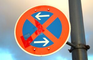 Parkvorschriften am Urlaubsziel beachten! Parkvorschriften in Urlaubsländern: Bild zeigt eine Halteverbotstafen und zwei entgegen zeigenden weißen Pfeilen auf blauem Hintergrund