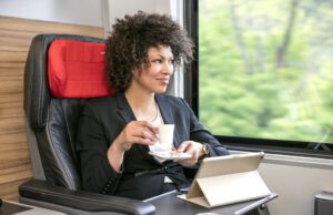 AIRail hebt jetzt im 30 Minuten-Takt ab AIRail im 30-Minutentakt. AIRail verbindet die Stadtzentren von Linz, Salzburg und Graz mit dem Flughafen Wien. Bild zeigt eine Frau mit Kaffeetasse in einem Zugabteil