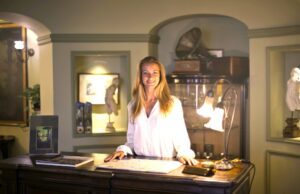 Hospitality Branche macht wieder Umsätze Tourismus unter Druck: Hotelrezeption, eine junge blonde Frau stecht hinter dem Desk, eine Leuchte spiegelt sich