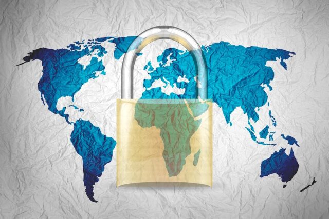 Cybersecurity auf Geschäftsreisen Bild zeiht die Weltkarte mit allen Kontinenten und ein gelbliches Sicherheitsschloss, dass das Thema Cybersecurity symbolisieren soll