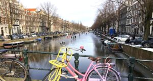 Nach Amsterdam mit Eurowings ab Salzburg Nach Amsterdam mit Eurowings ab Salzburg jetten. Zusehen ist eine vereist Gracht. Am Brückengeländer geht ein buntes Fahrrad. Auf der vereisten Gracht laufen Menschen Schlittschuh