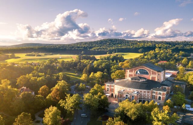 Bayreuther Festspiele Luftbildaufnahme zeigt das Festspielhaus in Bayreuth, umgeben von einem Wald im Nachmittagslicht