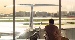 Kein Ärgernis, keine Ausgleichsleistung! Mann sitzt in der Wartehalle eines Flughafens und blickt hinaus aufs Rollfeld, wo ein Flugzeug steht