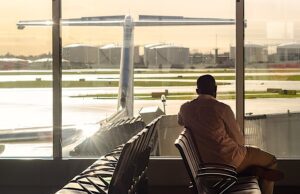 Kein Ärgernis, keine Ausgleichsleistung! Mann sitzt in der Wartehalle eines Flughafens und blickt hinaus aufs Rollfeld, wo ein Flugzeug steht
