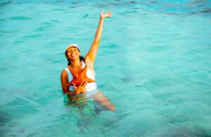 Frühbucher bringen Milliarden in die Kassen Frühbucher profitieren bei den Reisekosten: Frau im türkisfarbenen Meer streckt eine Hand zum Himmelt und mit der anderen hält sie einen roten Seestern vor dem Badekostüm