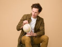 Österreicher entdecken wieder das Reisen Österreicher und ihr Reiseverhalten in 2024: Junger Mann hält einen Globus in der Hand und zeigt auf einen Erdteil