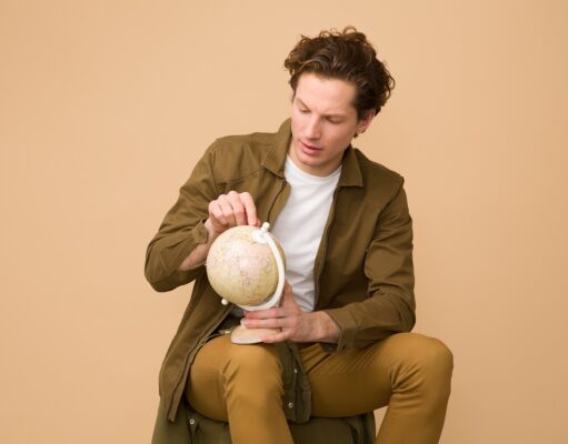 Österreicher entdecken wieder das Reisen Österreicher und ihr Reiseverhalten in 2024: Junger Mann hält einen Globus in der Hand und zeigt auf einen Erdteil