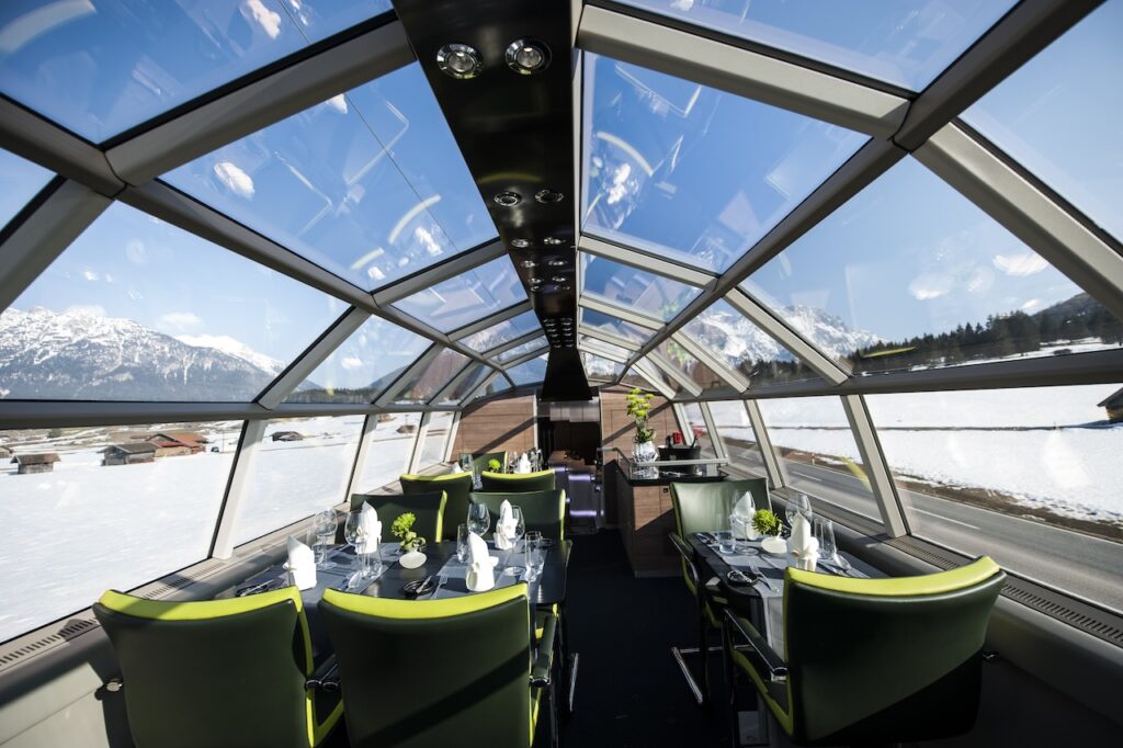 Panoramawagen im Luxuszug: Ausblick auf verschneite Landschaft, Berge und Ortschaften