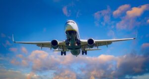 Flugreisen steuern auf neuen Höhepunkt zu Flugreisen im Aufwind: Passagierflugzeug im Steigflug, im Hintergrund blauer Himmel und rosafarbene Wolken