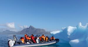 Arktis und Antarktis fliegen aus dem Katalog Kreuzfahrten in die Arktis und Antarktis: Ein Schlauchboot mit Kreuzfahrt-Touristen nähert sich einem strahlend weißen Gletscher