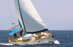 Trotz Bootsführerschein: Stress im Urlaub? Bootsführershein: Leicht zur Seite geneigtes weißes Segelschiff mit aufgeblähtem Segel unterwegs auf dunkelblauem Meer