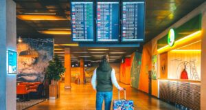 Urlaubsbudget heuer um 300 Euro geringer Mageres Urlaubsbudhet: Reisender in Jeans mit Koffer steht in der Abflughalle und blickt auf eine Anzeigetafel mit den Abflugzeiten der Airlines