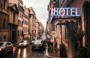 Für Hotelsterne gibt es 2025 neue Kriterien Neue Kriterienkatalog für Hotelsterne. Nasse Straße mit Autos und einem leuchtenden Hotelschild