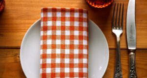 Gastronomie auf Suche nach neuen Ideen Holztisch mit rot-weiß karierter Serviette auf einem weißen Teller, rechts daneben Gabel und Messer aus Silber