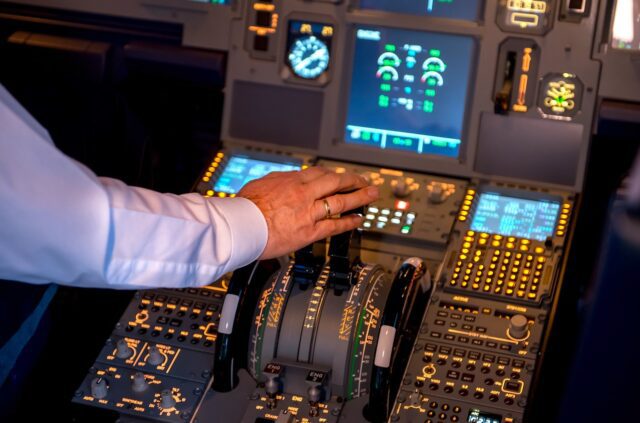Napping im Cockpit wegen Übermüdung gefährdet Flugsicherheit: Pilot im Cockpit greift nach Hebel. Beleuchtete Armaturen