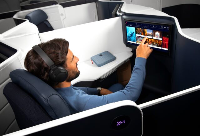 Mann sitzt in der Business Class von Air France und tippt mit dem Finger auf einen Bildschirm vor ihm, der auf der Rückseite des Vordersitzes integriert ist