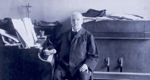 Anton Bruckner, der „fromme Revolutionär“ Der Komponist und Organist Anton Bruckner sitzt angelehnt an ein Klavier in seiner Wohnung