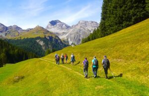 Gemeinsam wandern hilft gegen Einsamkeit Menschen wandern in einer grünen Alpenlandschaft in Richtung der Berge